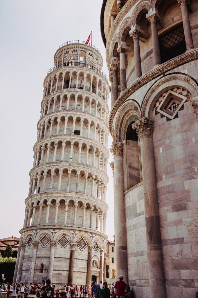 La Torre Pendente di Pisa accanto a un edificio storico, con turisti che ammirano la sua bellezza architettonica