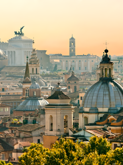 Vista panoramica dell’architettura storica di Roma, inclusi chiese a cupola e monumenti iconici, immersi nella calda luce dell’ora dorata.